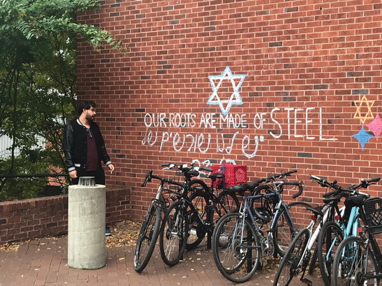 A student stands by a brick wall bearing the inscription "Our bones are made of steel" in chalk